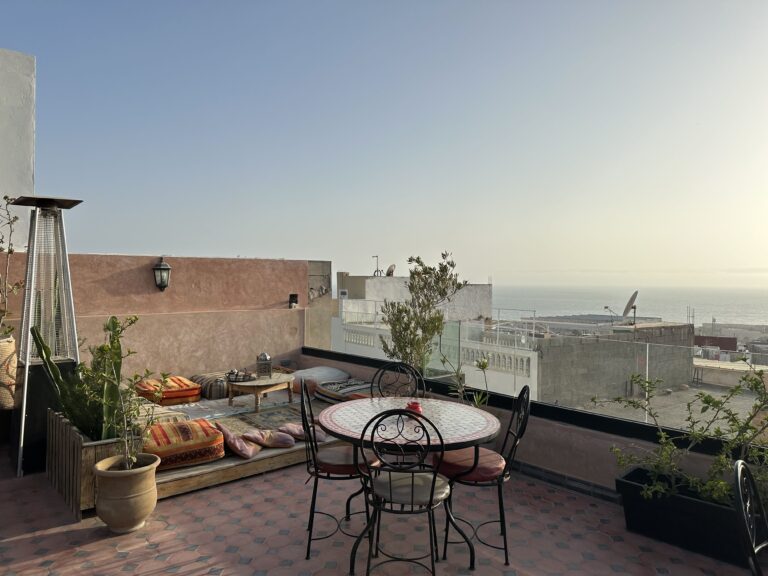 Vue d’une terrasse au Maroc avec des poufs typiques et l’océan en arrière-plan