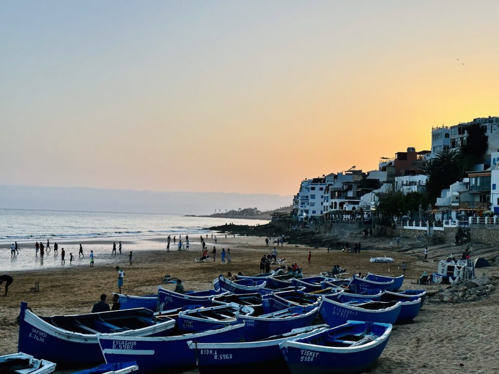 Kustdorp Taghazout met de typische blauwe boten van de regio en mensen op het strand.