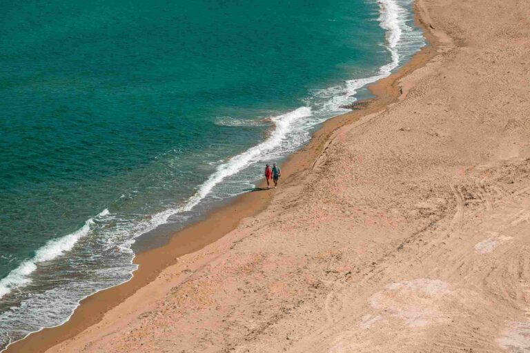 Two people walking on a beach by the sea, enjoying a peaceful moment.